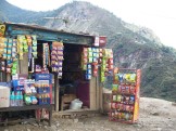 a small mountainside snack shack, with a display of potato chips on one side, bottled waters and juices out front, with clipped packages of snacks hanging on the outside of the shack